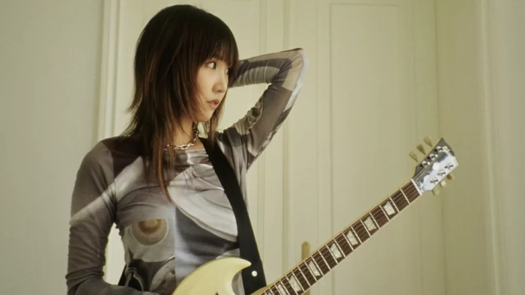 MEMI looking sideways, her guitar strapped to her body.